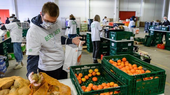 In einer Halle des Berliner Großmarkts packen ehrenamtliche Helfer der Berliner Tafel mit Atemschutzmasken Lebensmittel ein