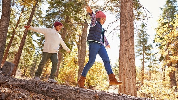 Zwei Kinder balancieren im Wald auf einem Baumstamm