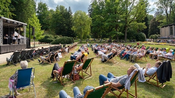 Publikum auf Liegestühlen von hinten mit Blick auf die Konzertbühne von German Brass im Kurpark von Bad Elster