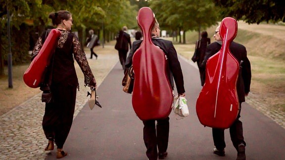 Mitglieder des MDR-Sinfonieorchesters gehen nach einem Konzert des MDR-Musiksommers in Magdeburg mit ihren Instrumentenkästen einen Weg entlang.