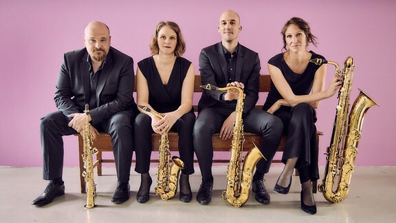 Zwei Musiker und zwei Musikerinnen des clair-obscur Saxophonquartetts mit Ihren Instrumenten auf einer Bank sitzend