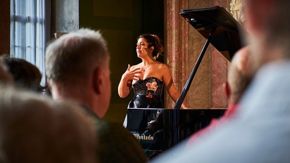Am Flügel stehende Pianistin Sophie Pacini moderiert vor dem lauschenden Konzertpublikum