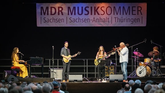 Nils Landgren sowie Alma Naidu und Band gemeinsam musizierend auf der Bühne in der Rotkäppchen Sektkellerei beim Konzert in Freyburg mit Rückansicht des Publikums