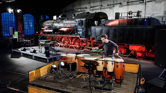 Schlagzeuger Johannes Fischer musiziert im Eisenbahnmuseum vor einer großen Lok.