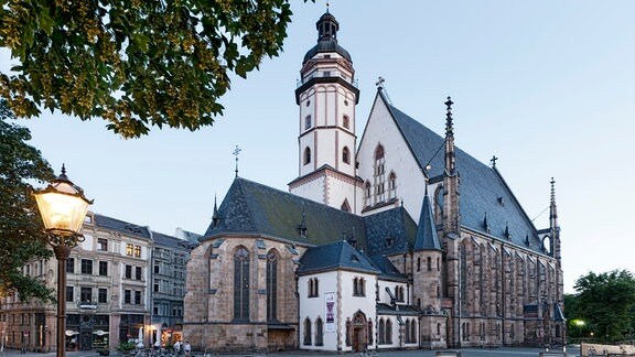 Die Thomaskirche in Leipzig, ein großer Turm, ein größeres Kirchenschiff und mehrere kleinere Gebäude daran
