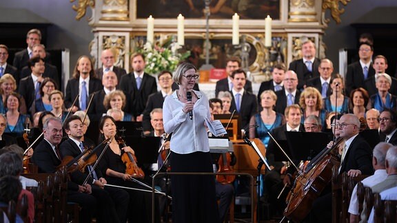 Chormanagerin Claudia Zschoch mit Mikro in der Hand vor den MDR-Ensembles in der St. Marienkirche in Marienberg