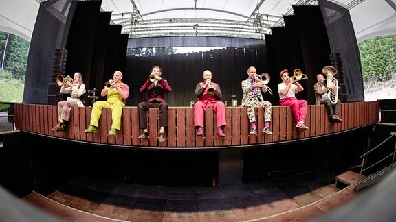 Das Blechblas-Ensemble Mnozil Brass sitzt auf dem vorderen Bühnenrand im Naturtheater Bad Elster beim MDR MUSIKSOMMER
