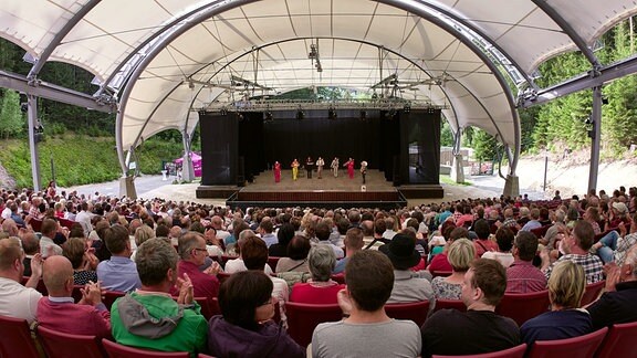 Blick über die Zuschauerreihen auf das Blechblas-Ensemble Mnozil Brass auf der Bühne im Naturtheater Bad Elster beim MDR MUSIKSOMMER.