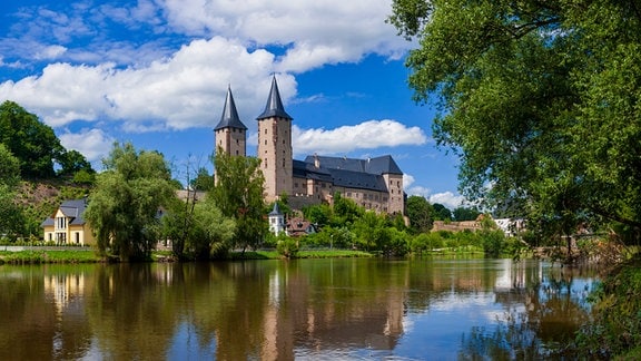 Blick auf das Schloss in Rochlitz über einen Fluss, das Schloss befindet sich auf der gegenüberliegenden Seite und spiegelt sich im Wasser. 