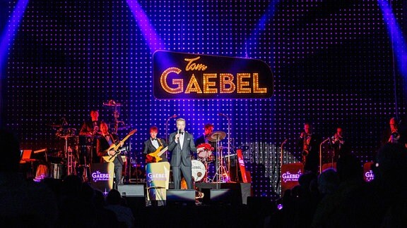 Sänger und Entertainer Tom Gaebel mit seiner Band auf der farbig beleuchteten Bühne in der Festhalle Ilmenau beim MDR-Musiksommer