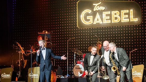 Sänger und Entertainer Tom Gaebel auf der Bühne in Ilmenau, wo neben ihm gerade seine drei Bläser gemeinsam in ein Mikrofon singen