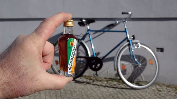 Ein Fahrrad, dvor eine Hand die eine Schnapsflasche hält