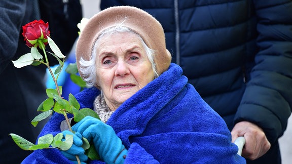 Eine Frau hält eine Rose bei einer Gedenkveranstaltung.