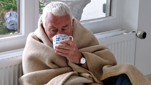 Illustration - Älterer Mann sitzt mit einer Tasse Tee und Decke frierend vor einer Heizung