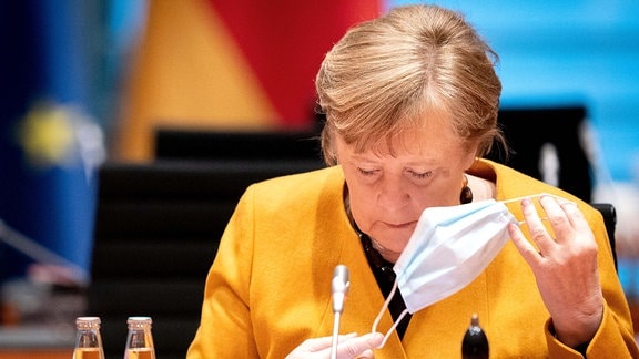 Kanzlerin Angela Merkel in gelber Jacke nimmt ihren Mundschutz ab, auf der wöchentlichen Sitzung des Bundeskabinetts im März 2021