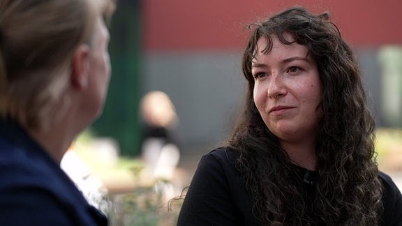 Eine Frau mitz dunklen Locken in einer Fußgängerzone im Interview