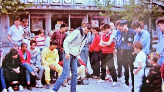 Zahlreiche Jugendliche stehen auf der Straße um einen Breakdancer.