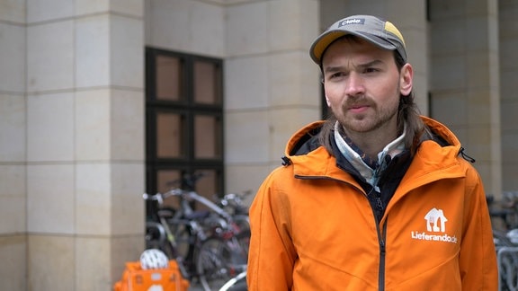 Marcus Heerlein mit einer orangenen Lieferando Jacke im Porträt. 