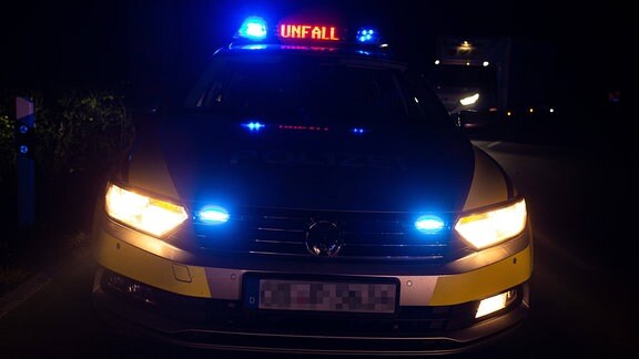 Ein Einsatzfahrzeug der Polizei in der Dunkelheit, mit Blaulicht und Schriftzug 'Unfall'
