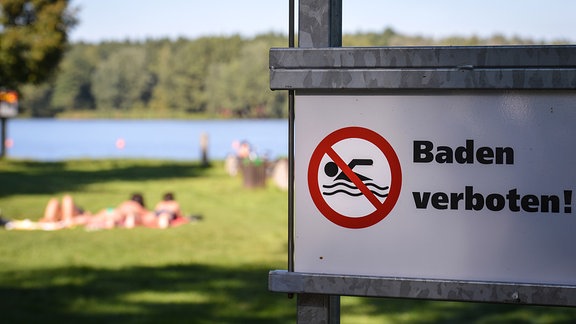 Ein Schild mit der Aufschrift Baden verboten steht am am Ufer eines Sees
