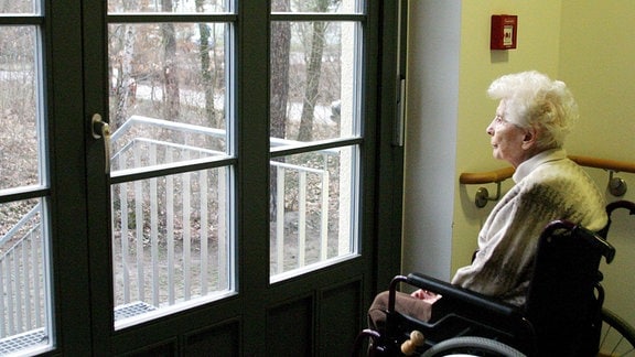 Eine Heimbewohnerin sitzt alleine am Fenster und schaut nach draussen.