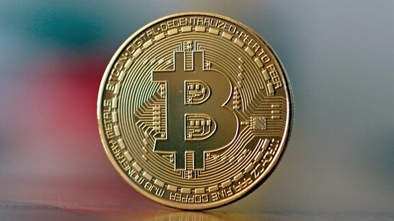 Eine Bitcoin Münze steht auf einem Tisch.