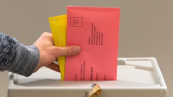 Ein Mann wirft im Wahllokal für die Briefwahl zwei Briefumschläge mit den Stimmzetteln in eine Wahlurne