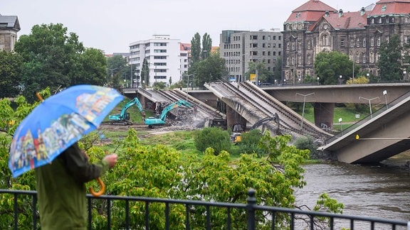 Ein Mann beobacht, wie Bagger weitere Teile der eingestürzten Carolabrücke in Dresden abreißen