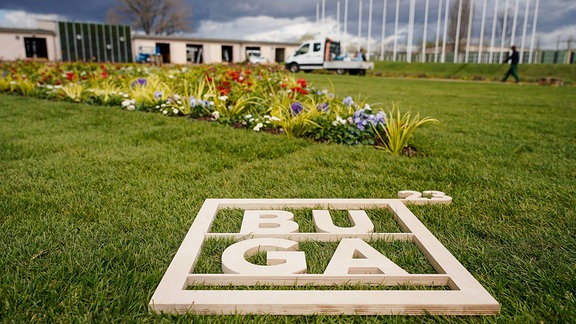 Ein Holzrahmen mit der Aufschrift „BUGA 23“ liegt auf dem Gelände der Bundesgartenschau vor einem Blumenbeet