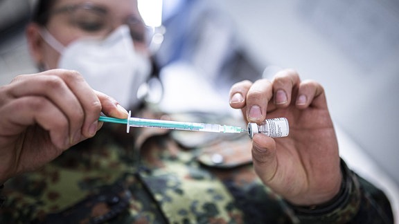 Eine Impfspritze wird durch eine Soldatin aufgezogen.