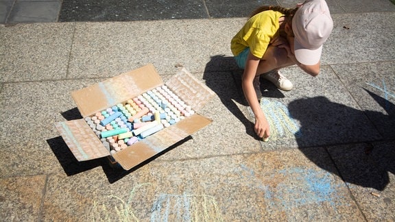 Kind mald mit blauer und gelber Kreide auf den Boden 