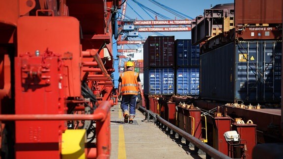Ein Mitarbeiter geht zwischen einer Containerbrücke und einem kleinen Containerschiff an der Kaimauer auf dem Gelände des Containerterminal Altenwerder (CTA). 