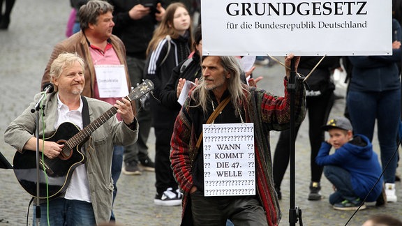 Liedermacher Gottfried Gunther Grimmer, rechts ein Demonstrant mit einem Schild 'Grundgesetz und Wann kommt die 47. Welle'