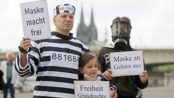 Bei einer Demonstration gegen Corona-Beschränkungen hält 2020 ein Demonstrant in gestreifter Kleidung, die der Uniform eines KZ-Häftlings nachempfunden ist ein Plakat mit dem Aufschrift "Maske Macht Frei" eine Anspielung auf den Spruch im Torbogen des Vernichtungslagers Auschwitz, "Arbeit macht frei".