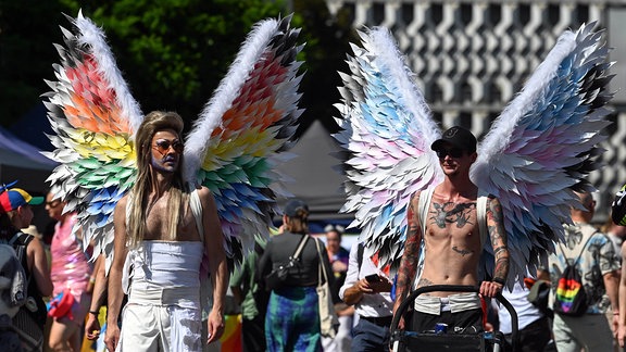 Teilnehmer gehen mit Flügeln in Regenbogenfarben und den Farben der Transfahne beim Christopher Street Day (CSD) durch die Innenstadt.