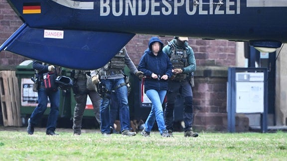 Eine Frau wird hinter einem Helikopter der Bundespolizeit abgeführt