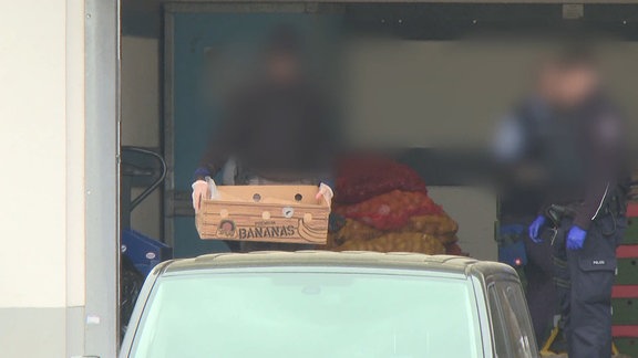 Verpixelte Gesichter: Polizisten verstauen Kisten und Säcke in einem Transporter hinter einem Supermarkt.