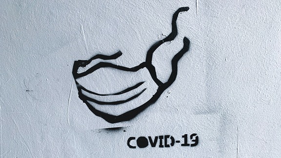 Schwarzes Graffiti eines Mund-Nasen-Schutzes auf einer weißen Wand.