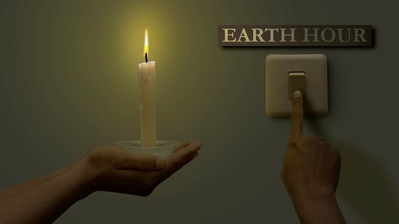 Eine Hand hält eine Kerze eine Andere Hand schaltet Lichschalter darüber ein Schild "Earth Hour"