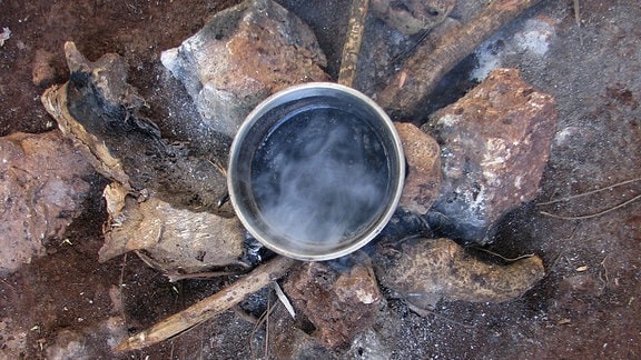 Einfache Feuerstelle aus Steinen in ländlicher Gegend, auf der eine Suppe erhitzt wird
