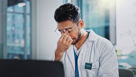 Arzt, Mann und müde mit Kopfschmerzen durch Laptop, Angst und Frustration im modernen Büro im Krankenhaus.