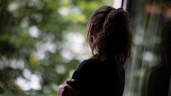 Eine Frau steht in einer Wohnung und schaut durch ein Fenster nach draußen.