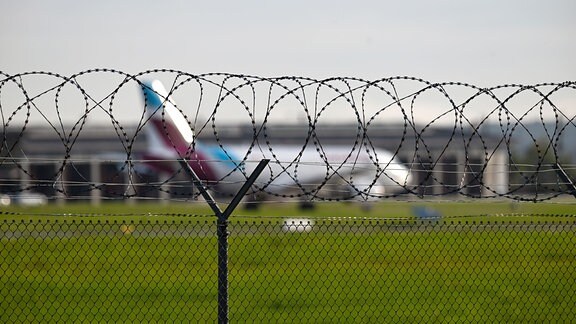 Zaun am Flughafen, im Hintergrund ein Flugzeug.