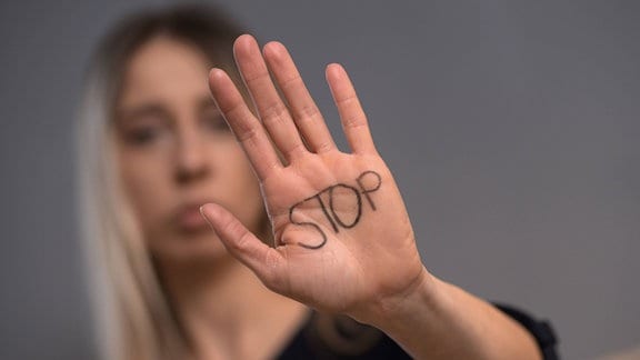 Eine Frau hebt die Hand, auf der STOP geschrieben steht.