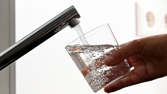 Eine Hand hält ein Glas unter einen laufenden Wasserhahn