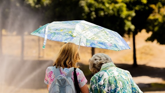 Zwei Frauen schützen sich mit einem Regenschirm vor der Sonne.