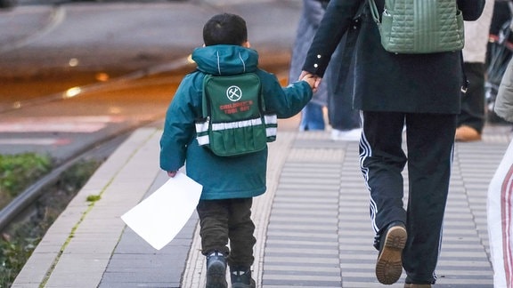Kind mit Rucksack an der Hand eines Erwachsenen