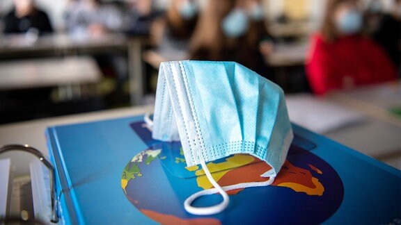 Ein Mund- und Nasentschutz liegt im Unterricht auf einem Weltatlas.