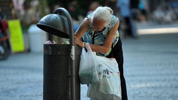 Im Müllbehälter sucht eine ältere Frau nach Pfandflaschen.