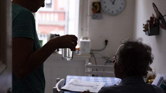 Pflegerin reicht Patienten ein Glas Wasser. 